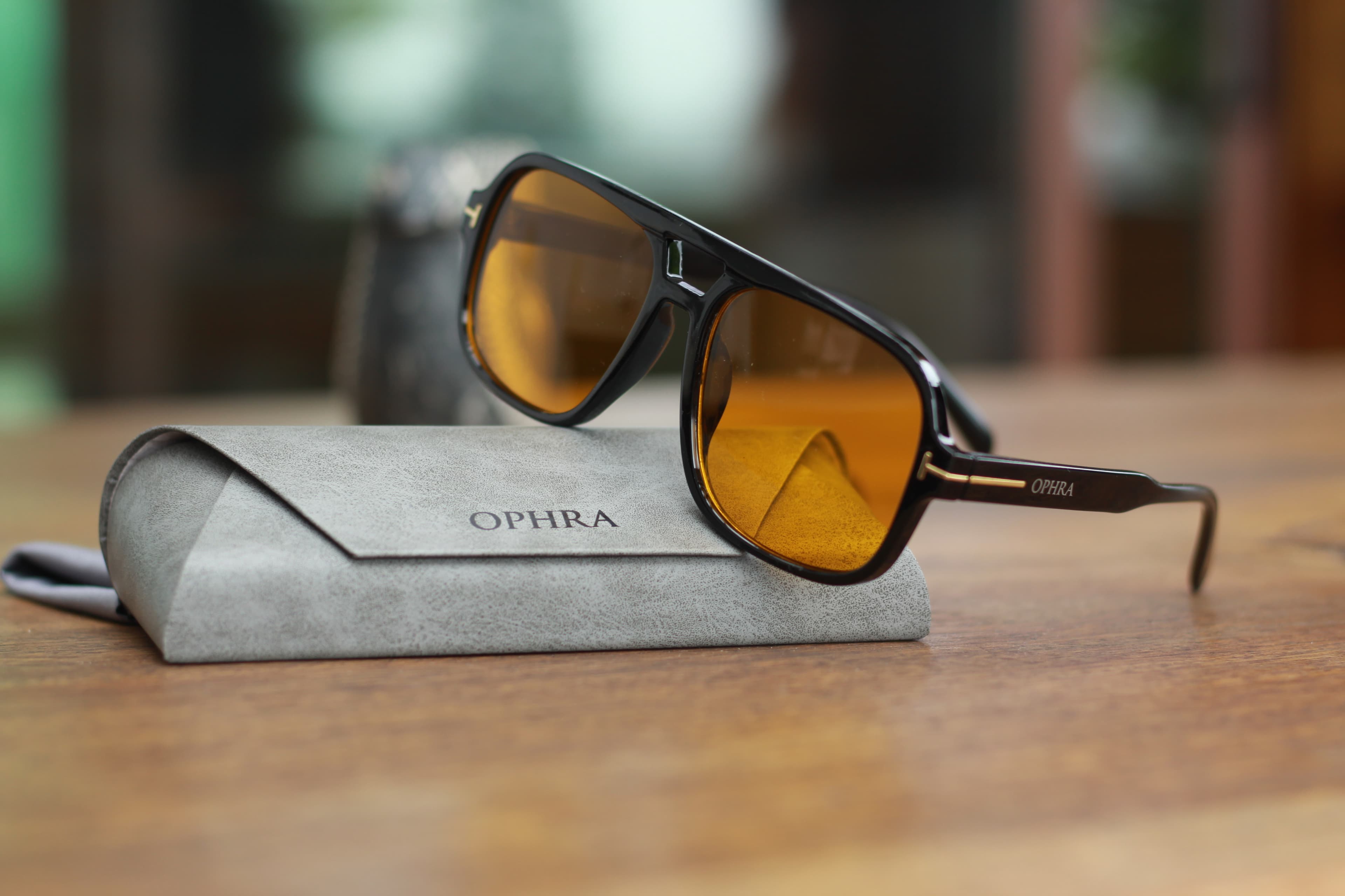 OPHRA amber-lensed aviator sunglasses on a suede case in warm light
