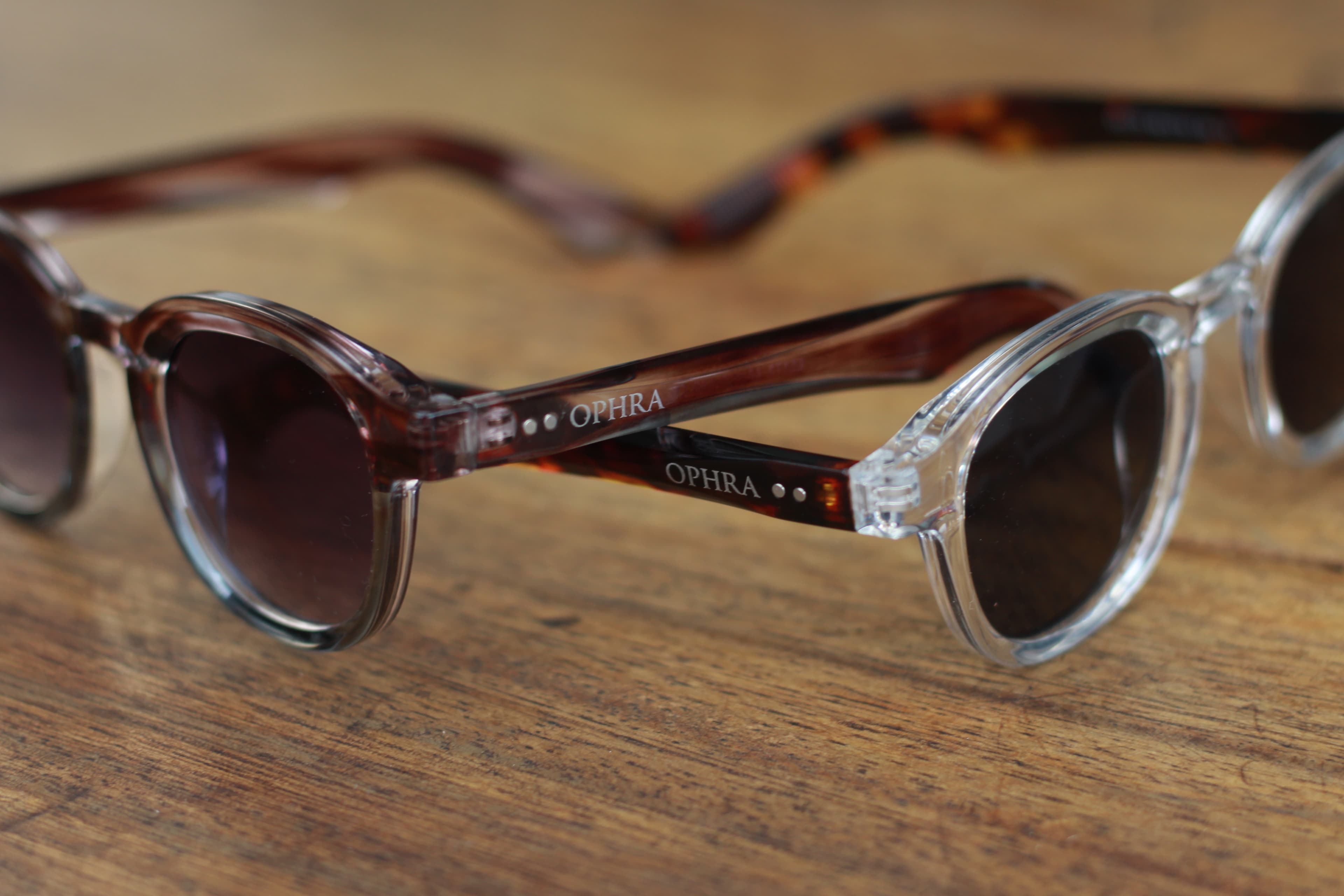 Detail of two OPHRA round-frame sunglasses on wood