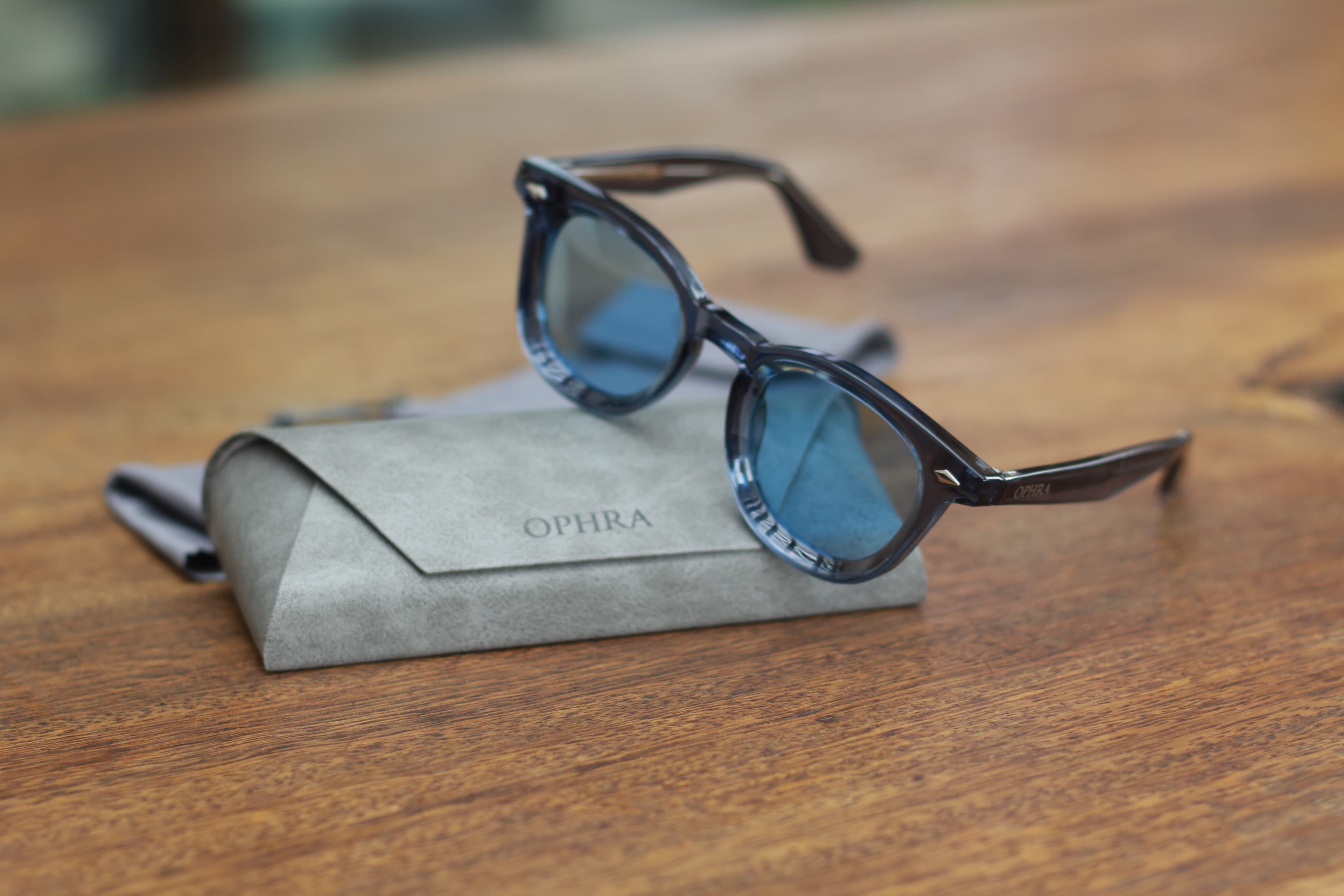 OPHRA round sunglasses with blue lenses on a suede case