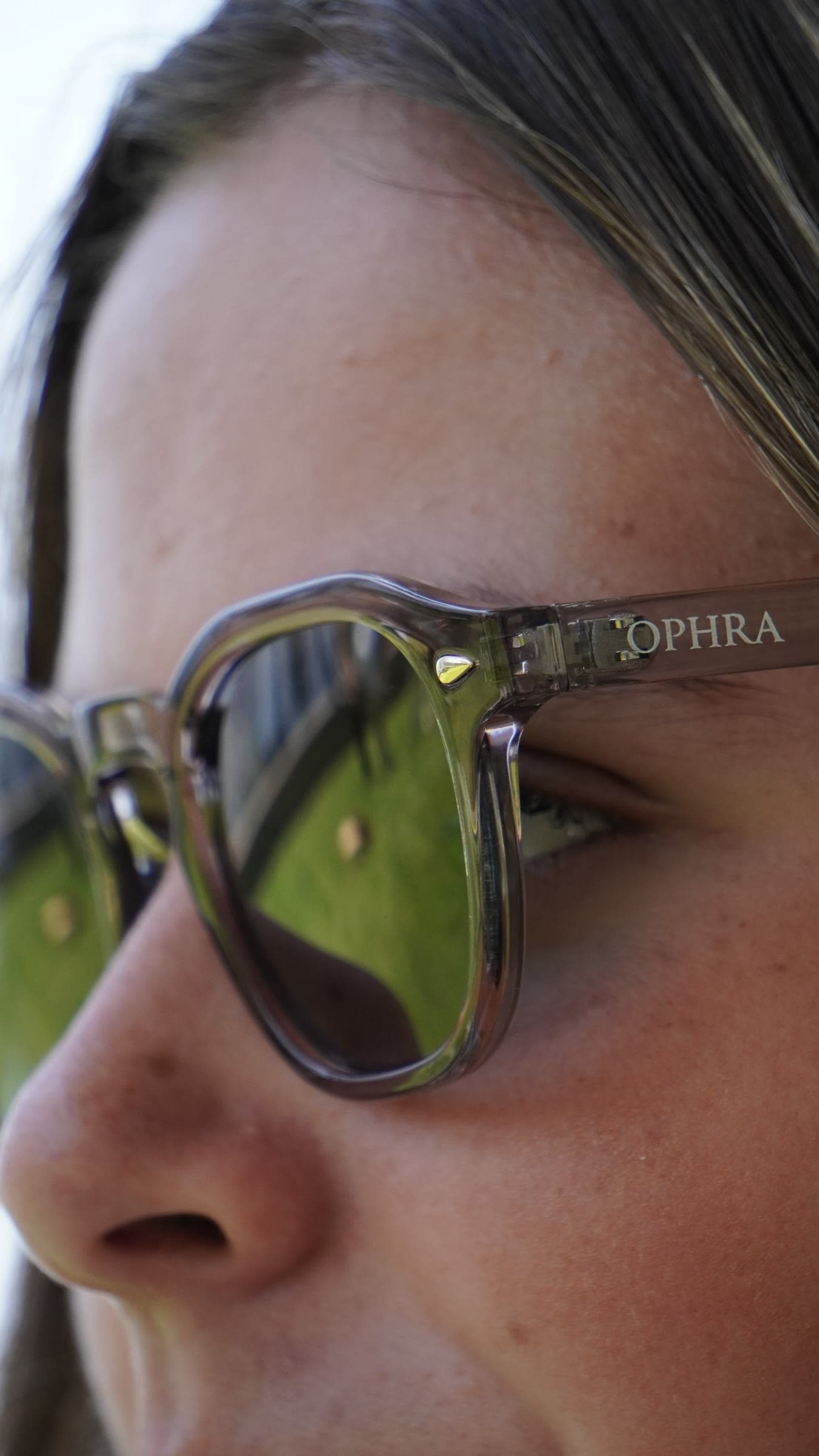 Close-up profile of a model wearing OPHRA translucent green-lens sunglasses